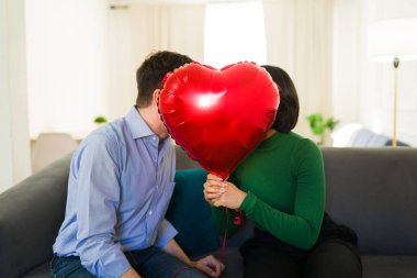 Sevgililer gününde evlerinde kırmızı kalp şeklinde bir balonla öpüşen tatlı bir çift.