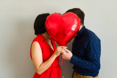 Sevgililer Günü 'nü kutlamak için öpüşmelerini kalp şeklinde bir balonun arkasına saklayan romantik çift.