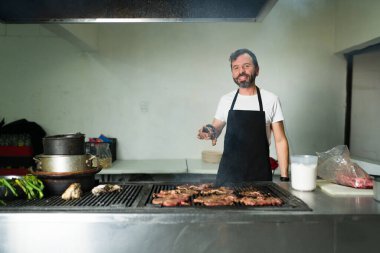 Lokanta mutfağında aşçı, gülümseyen bir gülümseme ile eti baharat ve ızgara yaparken leziz tacolar hazırlıyor ve mutfak uzmanlığını sergiliyor.
