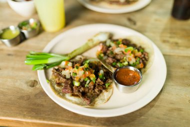 İki çekici taco, baharatlı salsa soslu bir tabakta servis edilir. Geleneksel Meksika Taqueria 'sında tadını çıkarmaya hazırdırlar.