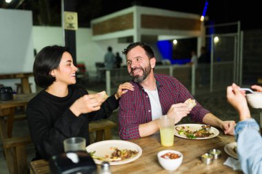 Happy friends are having dinner together, eating tacos and chatting at an outdoor mexican taqueria clipart