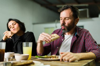 Meksika restoranında arkadaşlarıyla yemek yerken takosunun tadını çıkaran sakallı bir adam.