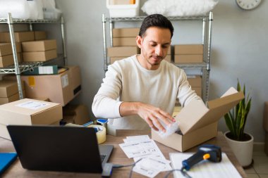 İspanyol adam karton kutular kullanarak küçük bir ofis veya depoda nakliye ve ambalaj ürünleri siparişi hazırlıyor.