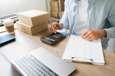 Küçük ecommerce işletme sahibi hesap makinesi kullanıyor ve lojistik belgelerini gözden geçiriyor, çevrimiçi mağaza siparişleri ve finansmanlarını yönetiyor
