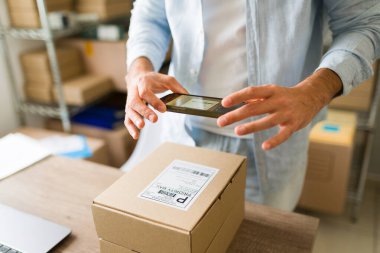 Karton kutudaki barkodları taramak için cep telefonu kullanan bir işletme sahibinin küçük şirket deposundaki siparişleri ve envanterleri yönetmesi.