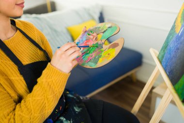 Bir ressamın, yaratıcı ifadeye dalmış, rahat stüdyosunda otururken paletine canlı renkler karıştırması.