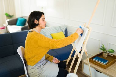 İspanyol kadın sanatçı, ev stüdyosunda çalışırken spatulayla dokulu resim yapıyor. Karışık medya sanatı tekniğiyle yaratıcılığını gösteriyor.