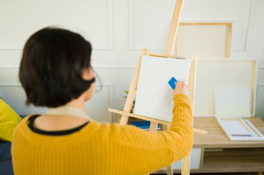 Kadın ressam, kişisel stüdyo alanında resim yaparken spatulayla desenli boya uyguluyor.