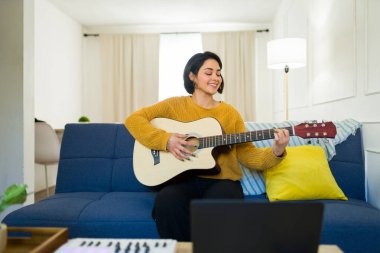 Mutlu İspanyol müzisyen kanepede oturup akustik gitar çalarken müzik kaydediyor ya da evde online ders çalışıyor.