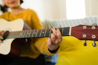 Evde akustik gitar çalan bayan bir müzisyenin yakın çekimi, orijinal bir şarkı besteleme sürecine dalmış.