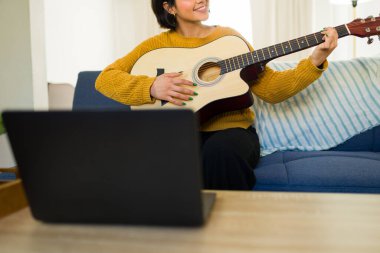 Kadın gitaristin çevrimiçi ders yoluyla müzik öğrenmesi, evde dizüstü bilgisayarla oturup akustik enstrüman çalışması.