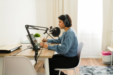 Dizüstü bilgisayar, profesyonel mikrofon ve kulaklık kullanarak evde çalışan ses podcast 'i kaydeden içerik yaratıcısının profil görünümü