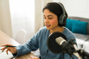 Profesyonel podcaster ses içeriğini kaydediyor, kulaklıkla mikrofona konuşuyor, ev stüdyosunda çalışıyor.