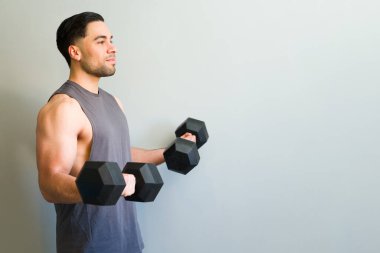 Formda bir gencin, kollarını ağırlıkla çalıştırıp, spor salonunda bisepsi kıvırırken profil görüntüsü.