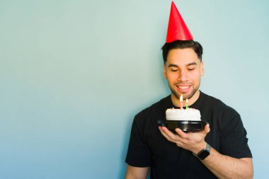 İspanyol genç adam doğum gününü küçük pasta ve mumlarla kutluyor, söndürmeden önce dilek tutuyor.