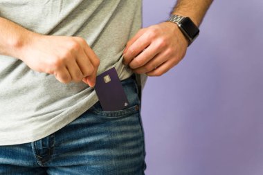 Kotunun cebine kredi kartı koyan bir adamın yakın plan fotoğrafı. Nakitsiz işlemleri ve kişisel finans yönetimini vurguluyor.