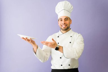 Yakışıklı İspanyol şef boş bir tabak sunuyor ve stüdyo içinde fotokopi alanı olan bir üniforma giyiyor.