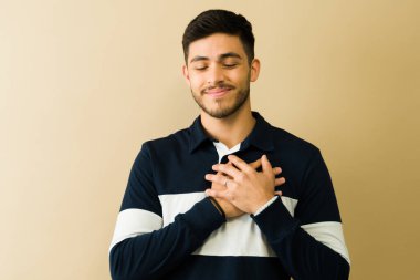 Minnettar genç adam gözleri kapalı gülümser ve ellerini göğsüne koyar. Minnettarlık ve minnettarlık hisseder.