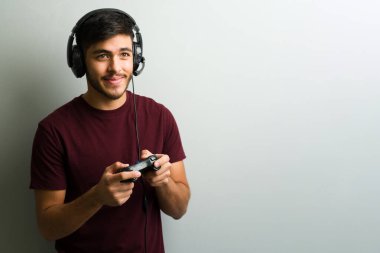 Genç bir İspanyol oyuncunun portresi. Kulaklık takıyor, kumanda tutuyor, video oyunları oynuyor ve eğleniyor.
