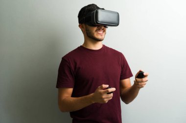 Genç adam video oyunu oynarken, video kulaklık takarken ve kablosuz kontrolörleri eğlence olsun diye kullanırken ilgi çekici bir deneyimden zevk alıyor.
