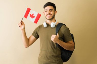 Sırt çantası ve kulaklık taşırken elinde küçük bir Kanada bayrağı tutan gülümseyen Latin bir öğrencinin portresi.