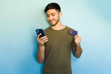 Erkek müşteri mavi arka planda online alışveriş için mobil bankacılık uygulaması ve kredi kartı kullanıyor