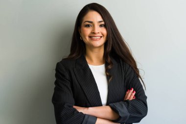 Kollarını kavuşturup takım elbise giyen neşeli bir iş kadınının portresi. Şirket ortamında güven ve profesyonellik yayıyor.