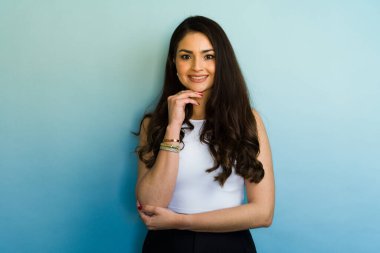 Güzel bir iş kadınının stüdyo portresi. Uzun kahverengi saçlı, elleri çenesinde, mavi bir arkaplanda gülümsüyor.