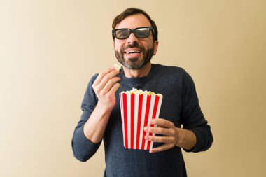 Heyecanlı adam 3D gözlük takıyor çizgili karton kovadan patlamış mısır yiyor ve gülümsüyor ve film seyrediyor.