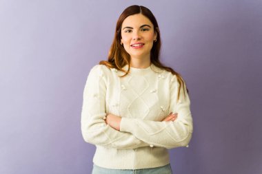 Kollarını kavuşturup gülümseyen neşeli genç bir kadının portresi, canlı mor bir arkaplan karşısında kendine güven ve pozitiflik yayıyor.
