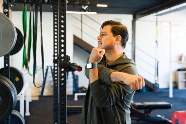 Kaslı erkek akıllı kasları kontrol ediyor, çağdaş egzersiz alanında yoğun fitness eğitimine hazırlanıyor.