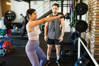 Çağdaş fitness merkezinde antrenör eşliğinde kettlebell salıncağı yapan bayan sporcu.
