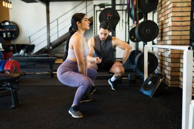 İspanyol kadın sağlık kulübü ortamında spor salonunu destekleyen profesyonel antrenörle ağırlıklı çömelme hareketleri yapıyor.