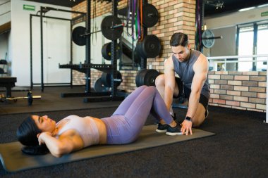 Kadın vücut kaslarını güçlendirirken, kişisel antrenör modern egzersiz tesisinde fitness antrenmanlarını fark ediyor ve rehberlik ediyor.