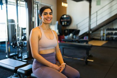 Terleyen fitness meraklısı yedek kulübesinde duruyor. Gösterişli ve çağdaş spor salonundaki yoğun egzersizden sonra gülümsüyor.