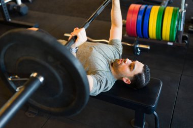 Spor salonunda ağırlık kaldıran güçlü bir adam, arka planda renkli plakalar olan kuvvet ve fitness antrenmanına odaklanıyor.