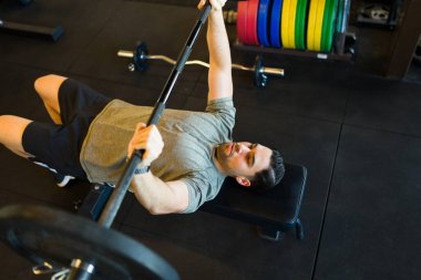 Spor salonundaki egzersiz sırasında kas gücü kazanmak için ağırlık kaldırırken halter kaldıran kararlı erkek sporcu.