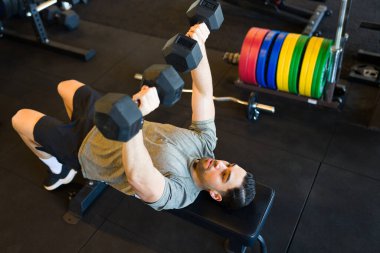 Güçlü İspanyol erkek halter seansı sırasında ağırlık kaldırıyor, çağdaş fitness merkezinde güçlü fiziği sergiliyor.