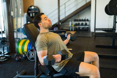 Dambıl egzersizi yapan güçlü bir sporcu. Çağdaş egzersiz tesisinin spor salonundaki spor salonunda oturuyor.