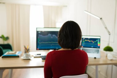 Finansal verileri inceleyen, birden fazla ekranı izleyen, piyasa eğilimlerini yoğun gayretle izleyen profesyonel bir kadın tüccar.