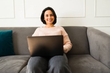 Evden çalışan, rahat bir şekilde kanepede otururken gülümseyen ve verimli iş günlerinde dizüstü bilgisayarda yazan serbest çalışan bir kadın.