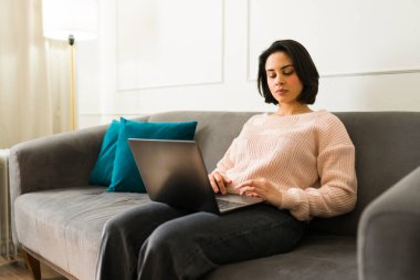Uzaktan kumandayla çalışan serbest çalışan kadın, profesyonel görev sırasında rahat bir kanepede dinlenirken dizüstü bilgisayara konsantre oluyor.