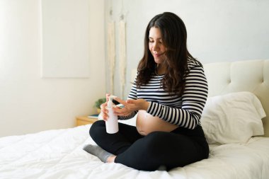 Hamile kadın karnına nazikçe nemlendirici krem sürüyor. Doğum öncesi cilt bakımı yapıyor.