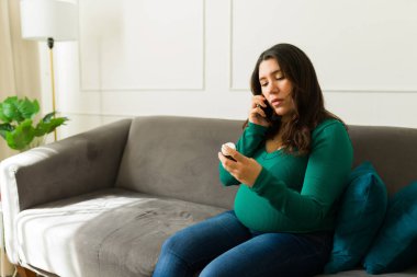 Ciddi hamile bir kadın, oturma odasında kanepede otururken doktorunu arayıp ilaçlarını tarif ediyor.