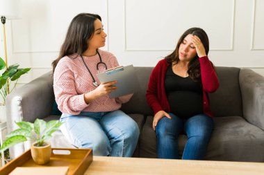 Tıbbi profesyonel hasta detayları, ev muayenesi sırasında baş ağrısı çeken hamile kadını dinlemek.