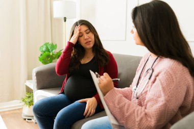 Hasta muayenesini belgeleyen kadın doktor, ev muayenesi sırasında baş ağrısı çeken hamile kadını kontrol ediyor.