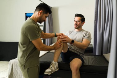 Çağdaş tıp merkezindeki rehabilitasyon sırasında erkek fizyoterapist hastaya diz masajı yapıyor.