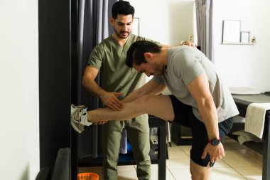 Latin hasta fizik tedavi sırasında bacak esneme ameliyatı oluyor, klinik rehabilitasyon ortamında profesyonel terapistle çalışıyor.