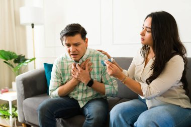 İspanyol kadın ortağını rahatlatıyor ve astım krizi sırasında ona astım ilacı veriyor. Evde kanepede otururken.