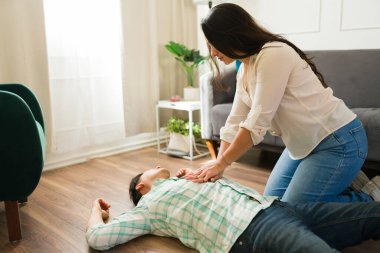 Evinde kalp krizi geçirdikten sonra yerde yatan baygın bir adama kardiyopulmoner resüsitasyon uygulayan İspanyol kadın.